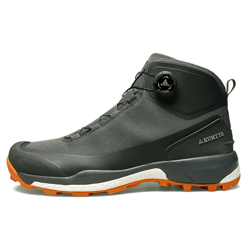 Les chaussures de randonnée Humtto HT-220838A pour hommes sont dotées d'une protection contre les éclaboussures, d'un système de laçage à cadran, d'un design gris et noir avec une bande de roulement orange, de logos visibles, et sont des chaussures de randonnée parfaites pour les sentiers accidentés.