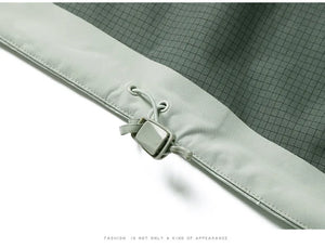 Gros plan sur l'ourlet d'une veste grise avec un cordon de serrage réglable et un bouton en plastique. Cette veste imperméable à coque dure, la Veste de randonnée "KUCLUT - Arder", vous assure d'être prêt pour les aventures de camping et de randonnée. Le texte en bas indique : "La mode n'est pas seulement une sorte d'apparence.