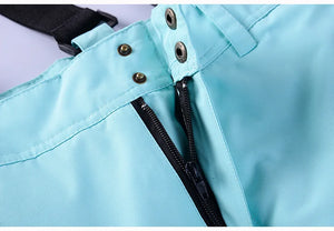 Vue détaillée du tissu polyester bleu clair doté d'une fermeture éclair noire distincte et de boutons-pression en métal de la combinaison de sports d'hiver « Artic King - Queen 105 » d'Artic King, conçue pour le ski, le snowboard et offrant une protection imperméable et coupe-vent pour les hommes et les femmes.