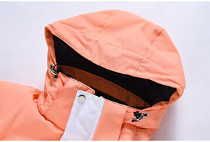 Gros plan d'une veste à capuche Artic King de couleur orange, avec une sangle boutonnée blanche et des détails d'œillets sur la capuche, fabriquée en polyester résistant. Le produit s'appelle "Combinaison d'hiver pour le ski, snowboard, imperméable et coupe-vent unisexe 'Artic King - Queen 105'.