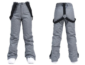 Vue avant et arrière de la combinaison d'hiver unisexe en polyester gris "Artic King - Queen 105" pour le ski et le snowboard, dotée de bretelles noires et complétée par des chaussures blanches, incarnant un style épuré et un confort.