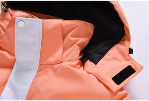 Gros plan de la veste en polyester orange « Artic King - Queen 105 », dotée d'un col haut et détaillée de boutons blancs, complétée par une sangle Velcro sur la capuche.