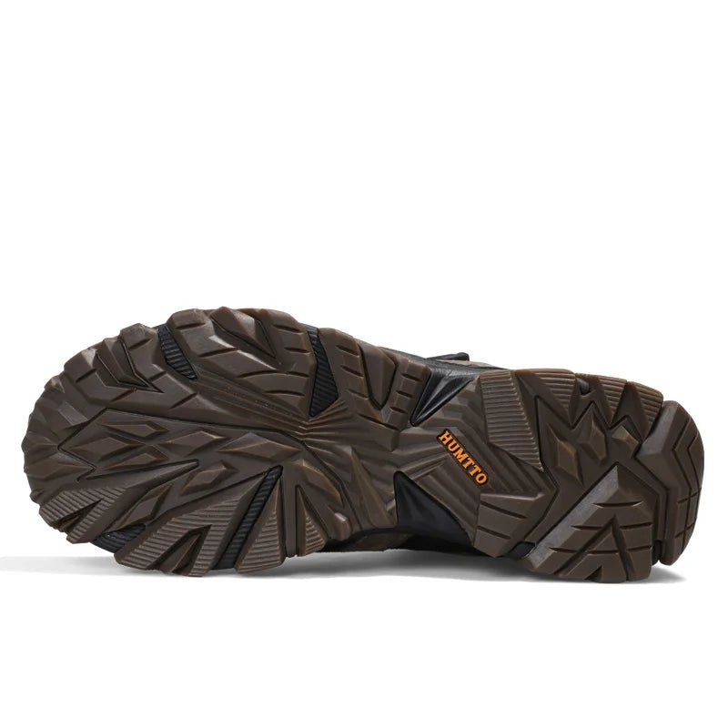 A pair of HUMTTO Chaussures de randonnée mid-top "HT-210626A" pour homme avec protection splash-proof, cuir véritable, semelle caoutchouc robuste, panneaux mesh et fermeture lacets, marron/noir avec accents verts, sur fond blanc.