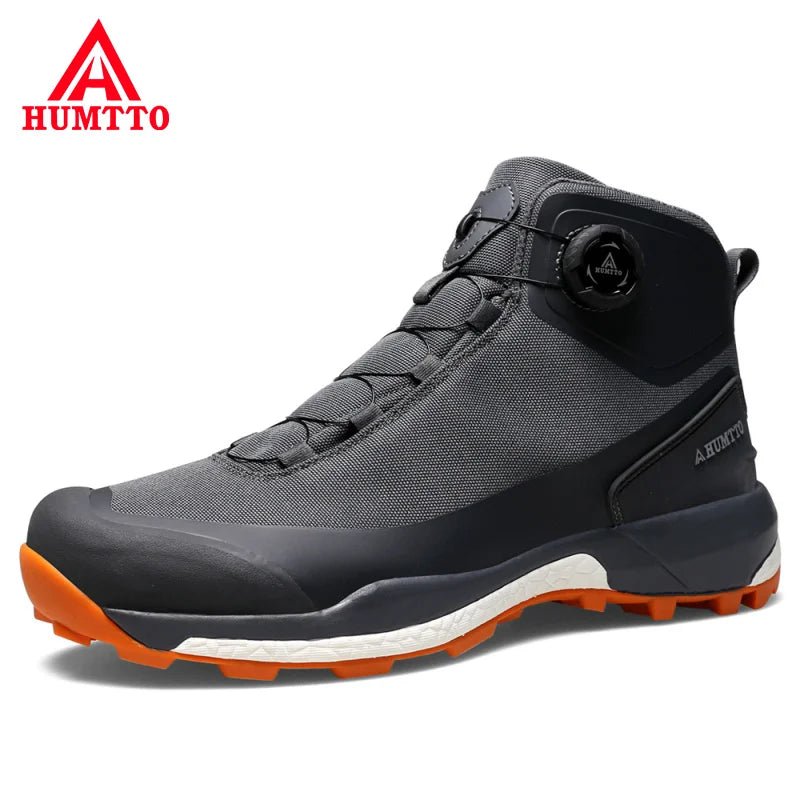 Les chaussures de randonnée Humtto HT-220838A pour hommes sont dotées d'une protection contre les éclaboussures, d'un système de laçage à cadran, d'un design gris et noir avec une bande de roulement orange, de logos visibles, et sont des chaussures de randonnée parfaites pour les sentiers accidentés.