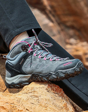 Les HUMTTO - HT-290027B mid-top randonnée bottines pour femme, en gris et noir avec accents roses, sont présentées en angle sur fond blanc. Elles offrent une protection splash-proof et une semelle antidérapante pour plus d'adhérence.