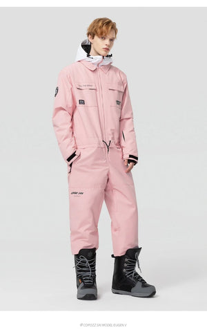 Personne en combinaison de ski Copozz Jump suit 21306 rose clair, bottes de snowboard grises et capuche blanche.