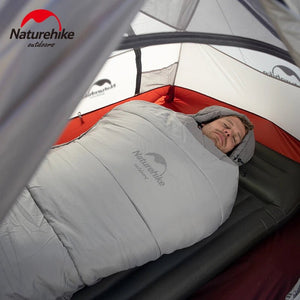 Quelqu'un dort confortablement sur un matelas gonflable dans une tente à l'intérieur d'un sac de couchage en coton imperméable Naturehike NH21MSD03 gris, adapté aux températures hivernales de +6°C.