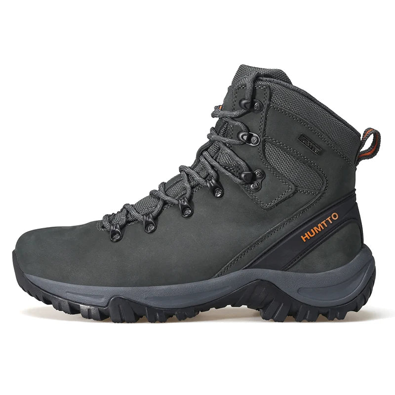 Les "HUMTTO - 230914A" sont des bottines d'alpinisme pour homme avec semelle grise, œillets métalliques, cuir véritable et logo "HUMTTO" orange, offrant une protection 100% imperméable pour la randonnée.