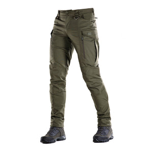 Un homme portant le pantalon M-TAC "M-Tac Conquistador Gen. I Flex" cargo tactique militaire résistant à l'usure et à l'eau, avec des poches utilitaires, et des chaussures noires à lacets, se tient les jambes écartées sur un fond blanc.