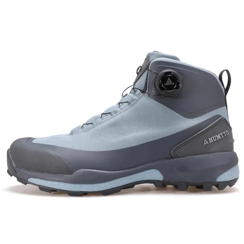 Les chaussures de randonnée Humtto HT-220838A pour hommes sont dotées d'une protection contre les éclaboussures, d'un système de laçage à cadran, d'un design gris et noir avec une bande de roulement orange, de logos visibles, et sont des chaussures de randonnée parfaites pour les sentiers accidentés.