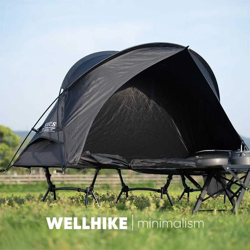 A Lit de camp 2 en 1 avec tente simple-paroi "Wellhike Minimalism - Yunchi SWS" de Wellhike Minimalism est installé sur l'herbe, avec des tables pliantes à proximité. Le texte "WELLHIKE minimalism" apparaît en bas de l'image.