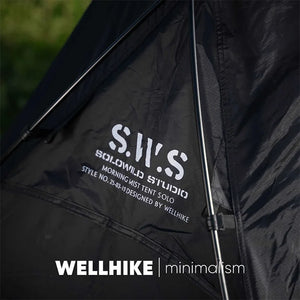 A Lit de camp 2 en 1 avec tente simple-paroi "Wellhike Minimalism - Yunchi SWS" de Wellhike Minimalism est installé sur l'herbe, avec des tables pliantes à proximité. Le texte "WELLHIKE minimalism" apparaît en bas de l'image.