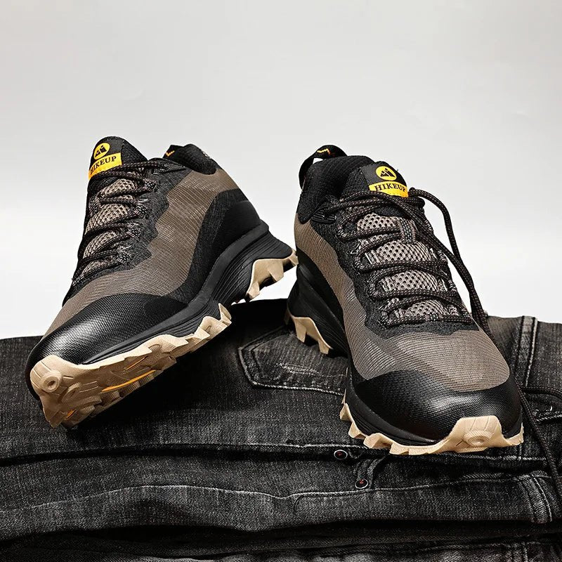 Chaussures de randonnée basses HIKEUP HK-15 noires et grises, semelles beiges, posées sur un jean denim, fond uni.