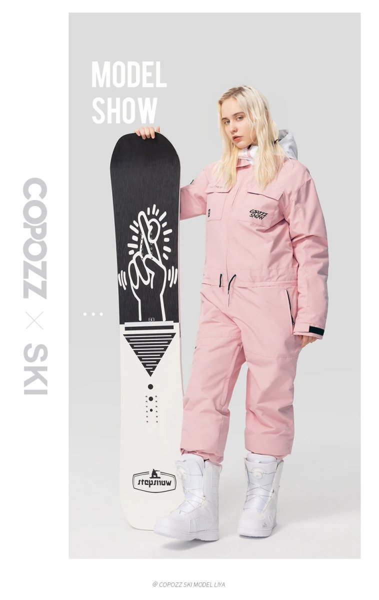 Femme en combinaison de ski imperméable Copozz rose clair 21306 et bottes blanches tenant un snowboard design.