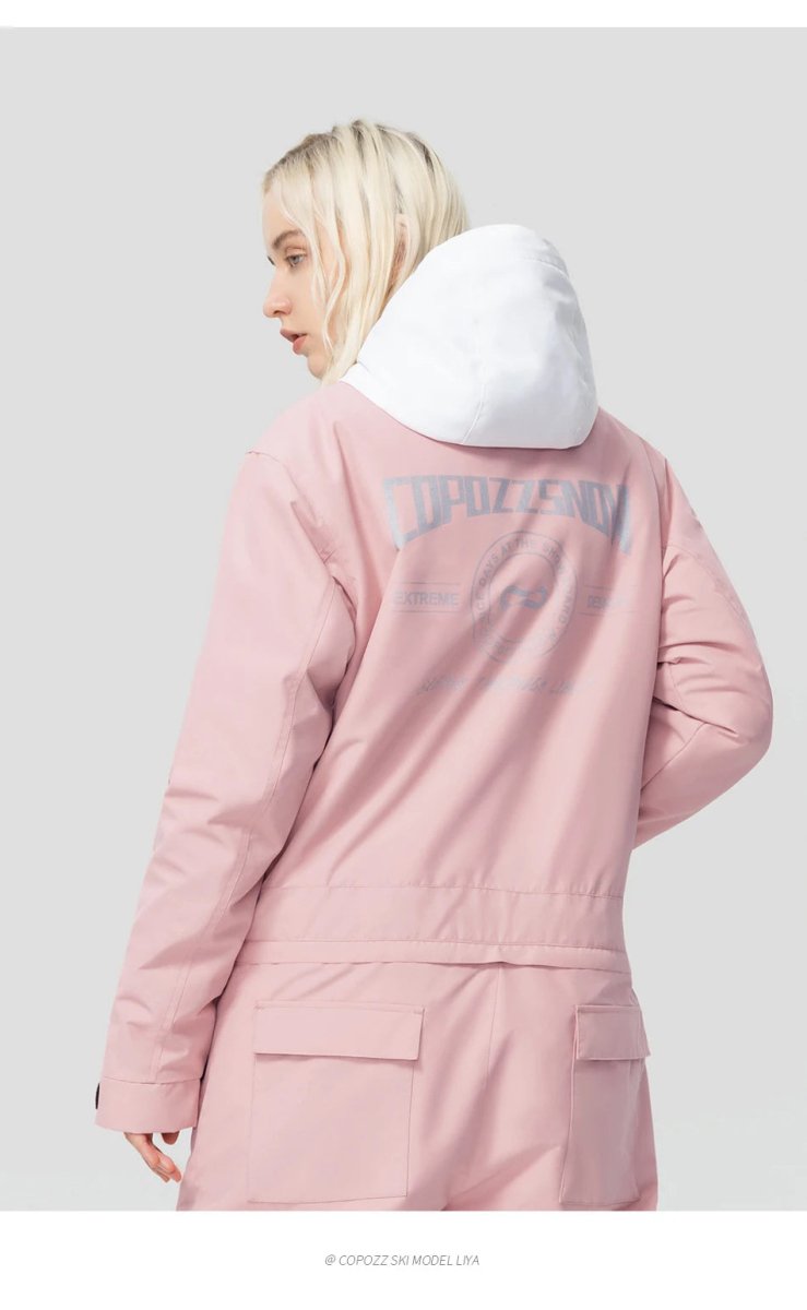 Personne blonde de dos en combinaison de ski Copozz Jump suit 21306 imperméable rose et blanche pour snowboarders.