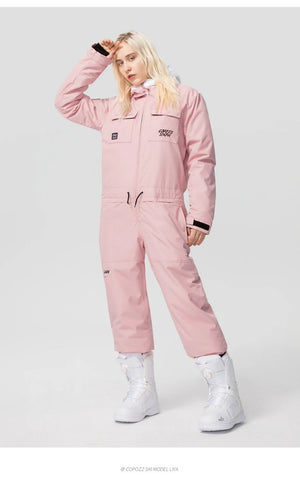 Personne portant la combinaison ski imperméable Copozz 21306 rose clair et bottes blanches, debout sur fond blanc.