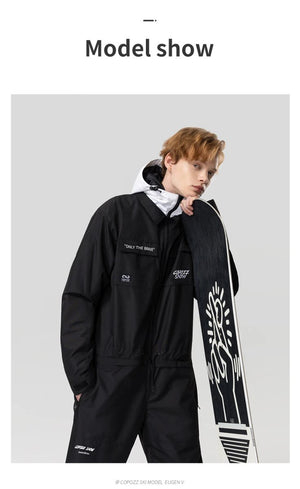 Personne aux cheveux châtains porte une combinaison de ski Copozz noire et blanche, tenant un snowboard, fond gris.