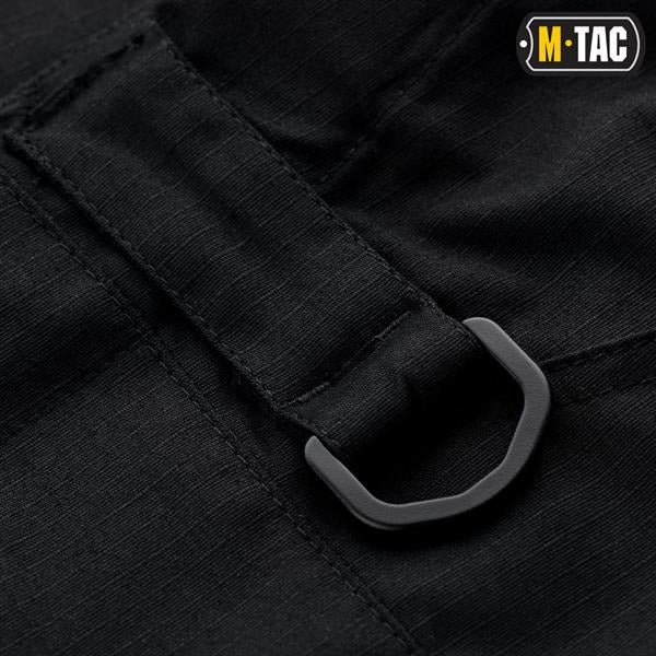 Un homme portant le pantalon M-TAC "M-Tac Conquistador Gen. I Flex" cargo tactique militaire résistant à l'usure et à l'eau, avec des poches utilitaires, et des chaussures noires à lacets, se tient les jambes écartées sur un fond blanc.