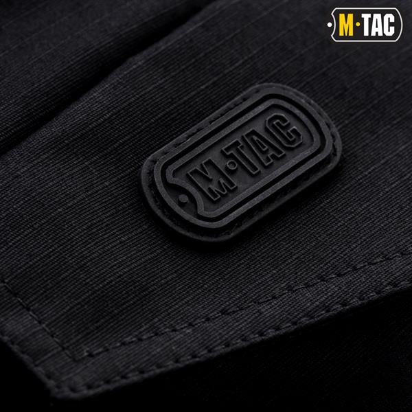 Un homme portant le pantalon M-TAC "M-Tac Conquistador Gen. I Flex" cargo tactique militaire résistant à l'usure et à l'eau, avec des poches utilitaires, et des chaussures noires à lacets, se tient les jambes écartées sur un fond blanc.